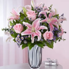 Pink lilies and roses in a glass vase with a small gift box