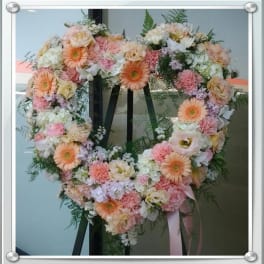Heart-shaped floral wreath with pink, peach, and white flowers on an easel
