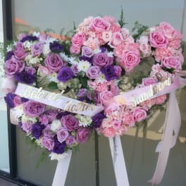 Heart-shaped floral tribute with pink and purple roses and ribbons