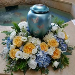 Floral funeral urn arrangement with yellow roses, white blooms, and blue hydrangeas