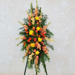Tall standing floral spray with roses and gladiolus in orange, yellow, and cream