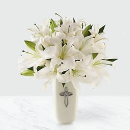 White lilies arranged in a tall cream vase with a cross emblem