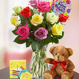 Bouquet of multicolored roses in a glass vase with a teddy bear and birthday card