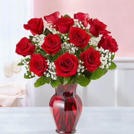 Red roses arranged in a red glass vase with white filler flowers