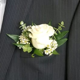 White rose boutonniere with small white filler flowers and greenery
