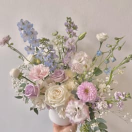 Pastel bouquet of roses, lisianthus, and blue delphinium in a white vase