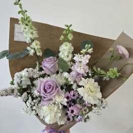 Hand-tied bouquet of lavender roses and white flowers wrapped in brown paper