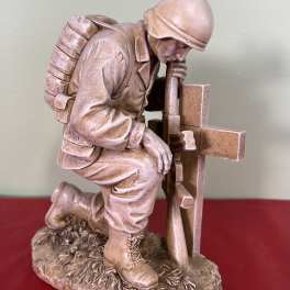 Stone soldier kneeling beside a cross memorial statue