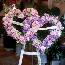 Two heart-shaped floral wreaths of pink and lavender roses on easels