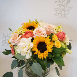 Bouquet of sunflowers, roses, and hydrangeas in a glass vase