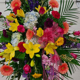 Large standing floral spray with bright mixed blooms and pink ribbon