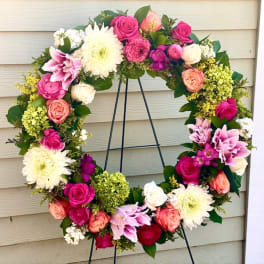 Heart-shaped floral wreath with pink, white, and peach blooms on a black stand