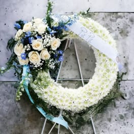 White floral funeral wreath with roses and blue accents on a stand