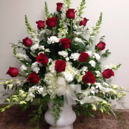 Tall arrangement of red roses and white flowers in a white vase with a sheer ribbon