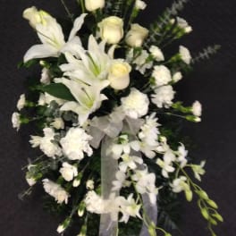 White floral spray with lilies, roses, and orchids on a dark background