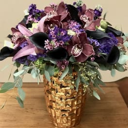 Bouquet of purple orchids and black calla lilies in a gold vase