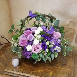 Purple and white rose arrangement in a wicker basket with ivy and butterfly accents