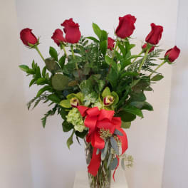 Red roses and green orchids in a glass vase with a red ribbon