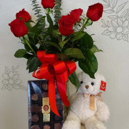 Red roses in a glass vase with a teddy bear and chocolate box