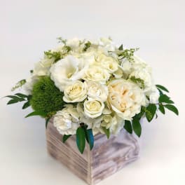 White floral arrangement in a wooden box with green accents