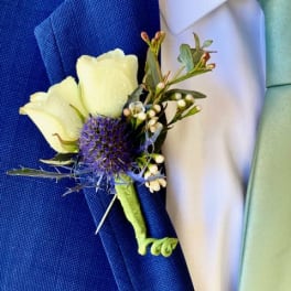 White boutonniere with a purple thistle bloom on a blue suit lapel