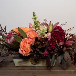 Low floral centerpiece with peach, burgundy, and green blooms in a rectangular container