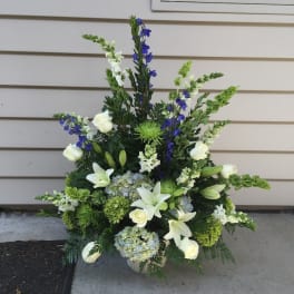 Tall floral arrangement with white lilies, roses, blue flowers, and green accents