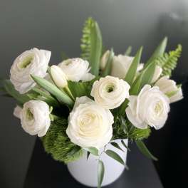 White ranunculus and roses arranged in a white vase