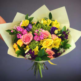 Mixed bouquet of pink, yellow, purple, and green flowers wrapped in pale paper