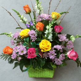 Mixed bouquet of roses and purple daisies in a green basket