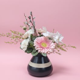Pink and white flowers arranged in a black vase with a beige stripe