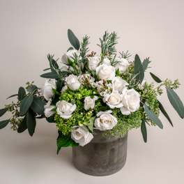 White roses in a gray vase with eucalyptus and green filler flowers