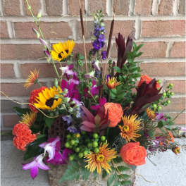 Mixed bouquet with sunflowers, roses, and purple blooms in a stone container