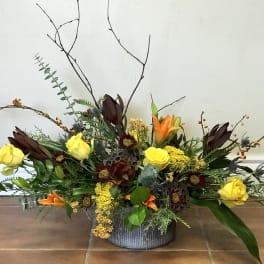 Low floral arrangement with yellow roses and orange lilies in a gray container