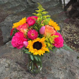 Bright mixed bouquet in a clear glass vase with sunflowers, roses, and pink blooms.