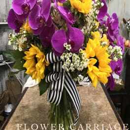 Bouquet of purple orchids and yellow sunflowers in a glass vase with a striped ribbon