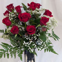 Red roses arranged in a tall silver vase with white baby's breath