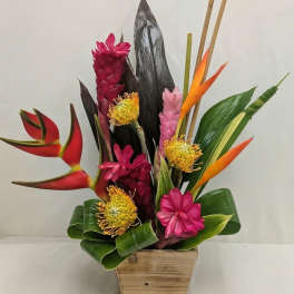 Tropical flower arrangement in a wooden container with pink, orange, and yellow blooms