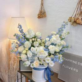 White and blue flower arrangement in a round box with a ribbon