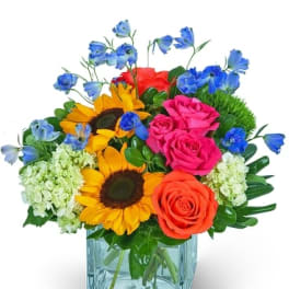 Colorful bouquet of roses, sunflowers, and blue flowers in a glass vase