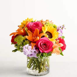 Colorful bouquet of roses, lilies, and sunflowers in a clear glass vase