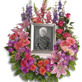 Standing floral wreath around a framed portrait with pink and purple flowers