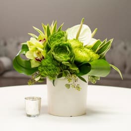 Green floral arrangement in a white vase with orchids and anthurium