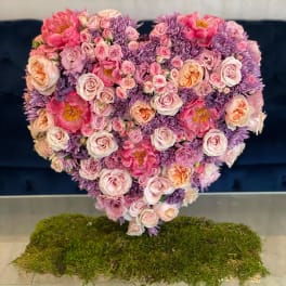 Heart-shaped bouquet of pink and purple flowers on a moss base