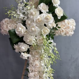 Large cross-shaped floral arrangement of white and blush roses with cascading orchids
