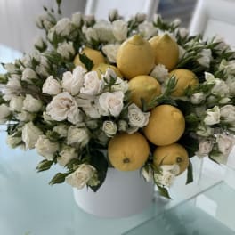 White roses arranged with lemons in a white vase