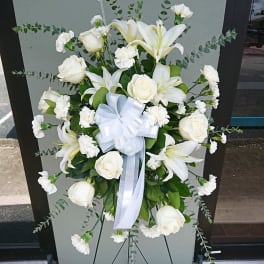 White floral standing spray with roses, lilies, and carnations on an easel