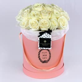 Cream roses arranged in a pink hat box with a ribbon tag