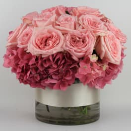 Pink roses and hydrangeas arranged in a glass vase with a ribbon band