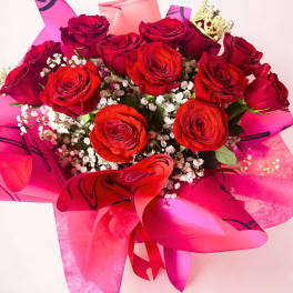 Bouquet of red roses with baby's breath and pink wrapping, topped with a small crown